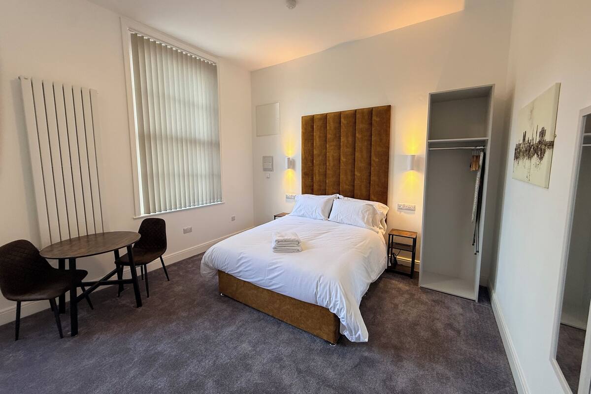 Una habitación de hotel con una cama, un escritorio, dos sillas, un armario y un radiador.