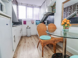 Una cocina compacta con una mesa de comedor, sillas de mimbre, una mesa de vidrio y una planta en maceta.