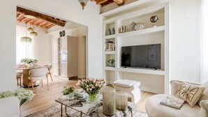 Ein modernes Wohnzimmer mit Fernseher, weißen Regalen, einer Essecke und einer Küche.