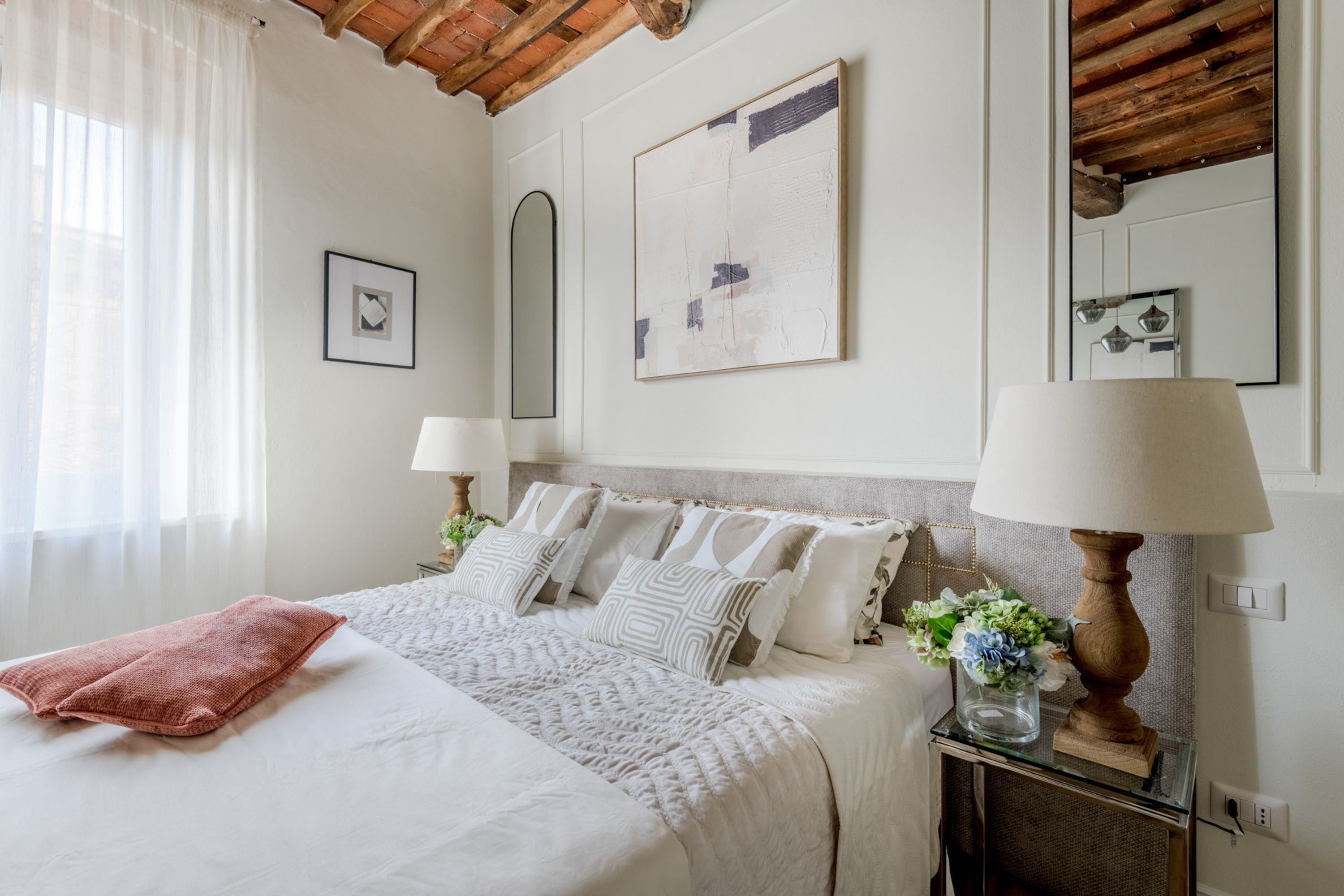 Un dormitorio con una cama, dos mesitas de noche, un espejo y una ventana con cortinas.