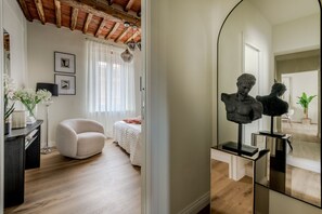 Un dormitorio con cama, una silla, un escritorio, un espejo y una escultura.