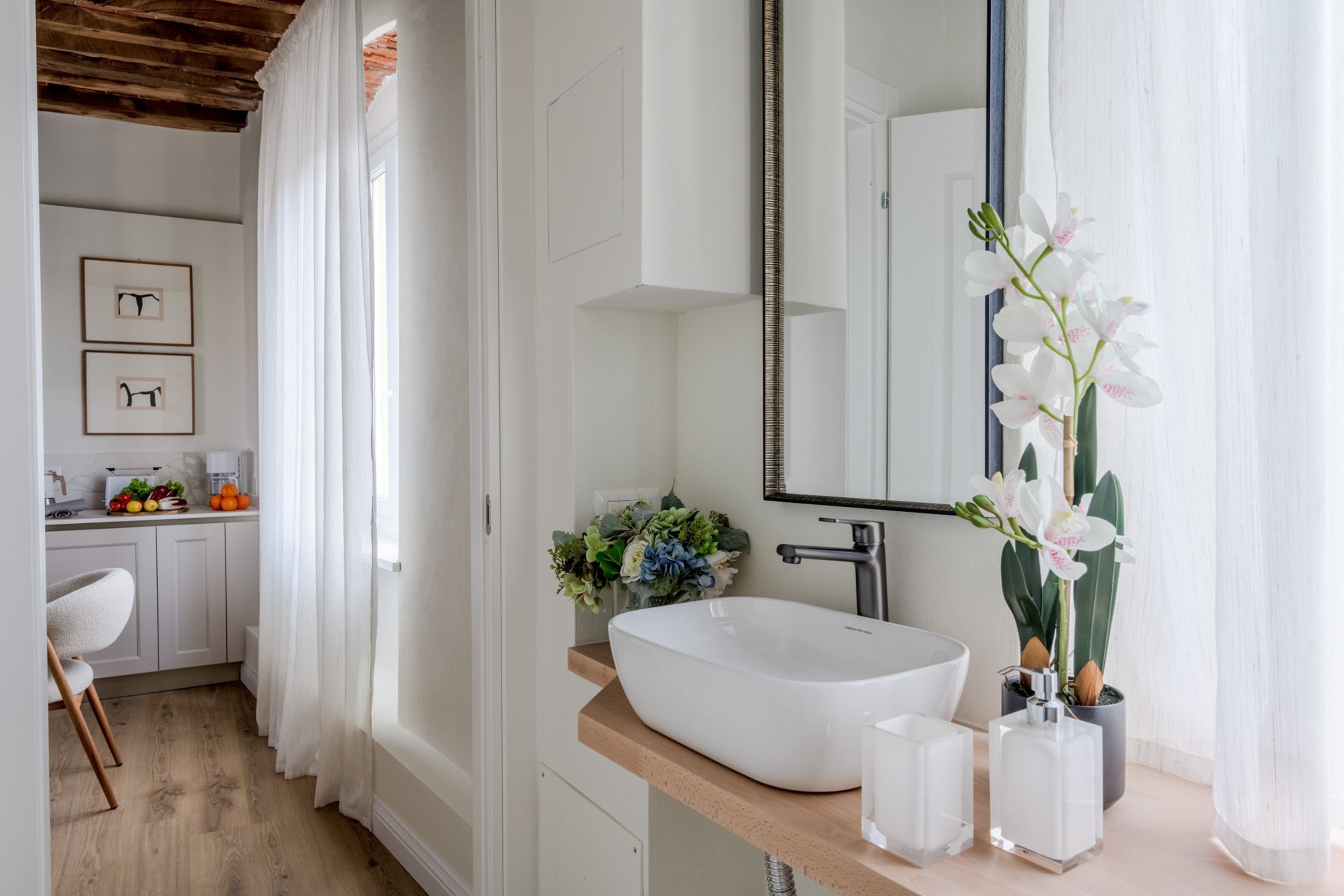 A modern bathroom with a large mirror, white sink, and a potted orchid.