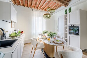 Una cocina moderna con armarios blancos, techo de madera y comedor con una mesa redonda para cuatro.
