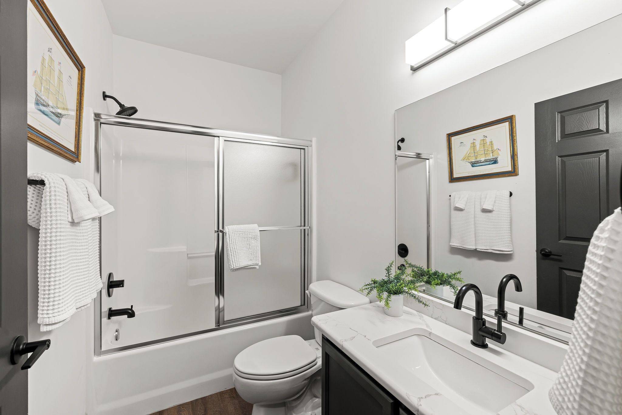 A modern bathroom with a glass-enclosed shower, a white toilet, a sink with a mirror, and a door with a dark frame.