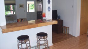 Una cucina con un piano di lavoro in legno, due sgabelli da bar, un frigorifero e una porta che dà su un'altra stanza.