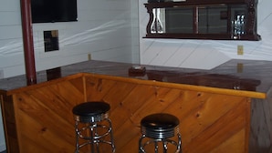 Angolo bar con sgabelli di legno, un bancone in legno e un televisore a parete.