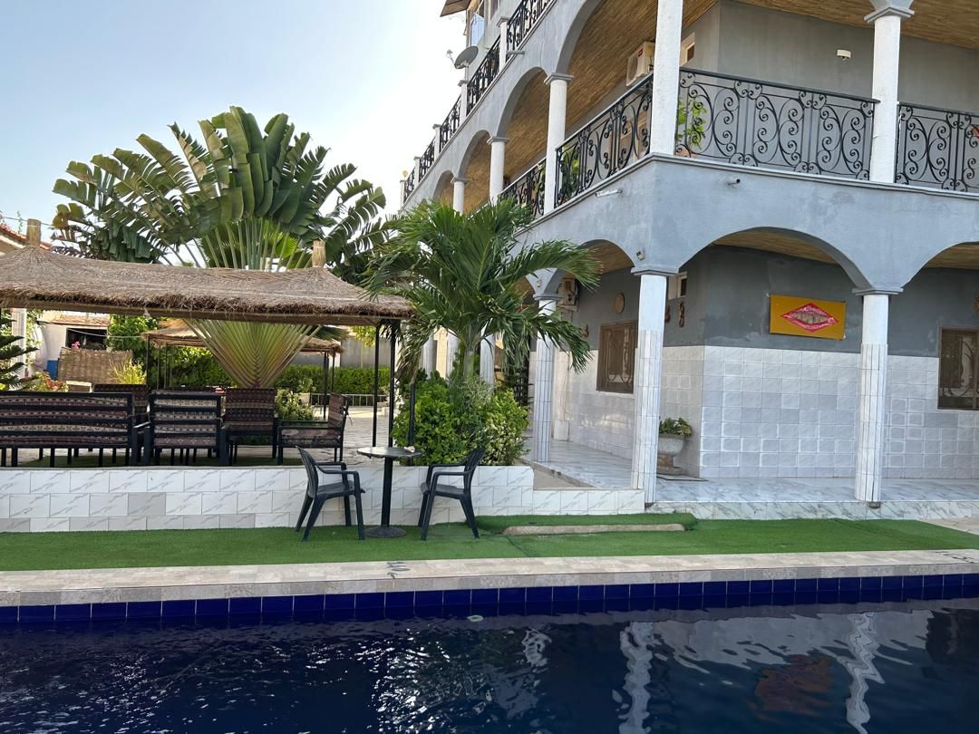 Un hotel con piscina, asientos exteriores y una zona cubierta con techo de paja.