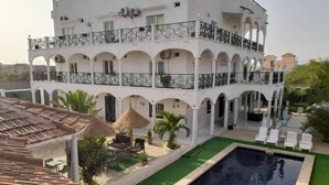 A multi-story building with a swimming pool, outdoor seating, and a covered patio area. - Jozene House  (Ngaparou)