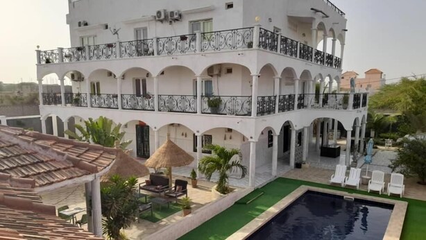 A multi-story building with a swimming pool, outdoor seating, and a covered patio area. - Jozene House  (Ngaparou)