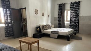 A bedroom with a bed, a sofa, a wooden table, and a bathroom visible through an open door. - Jozene House  (Ngaparou)