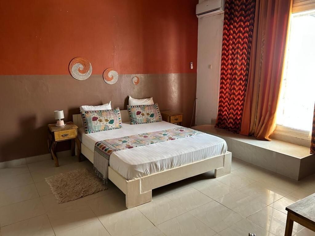 A bedroom with a bed, bedside tables, a window with curtains, and a wall-mounted air conditioner.