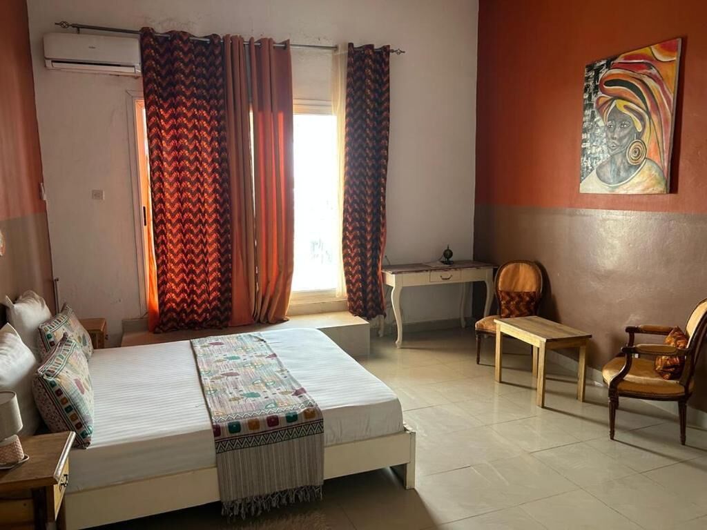 A bedroom with a bed, a desk, two chairs, and a painting on the wall.