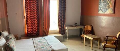 A bedroom with a bed, a desk, two chairs, and a painting on the wall.