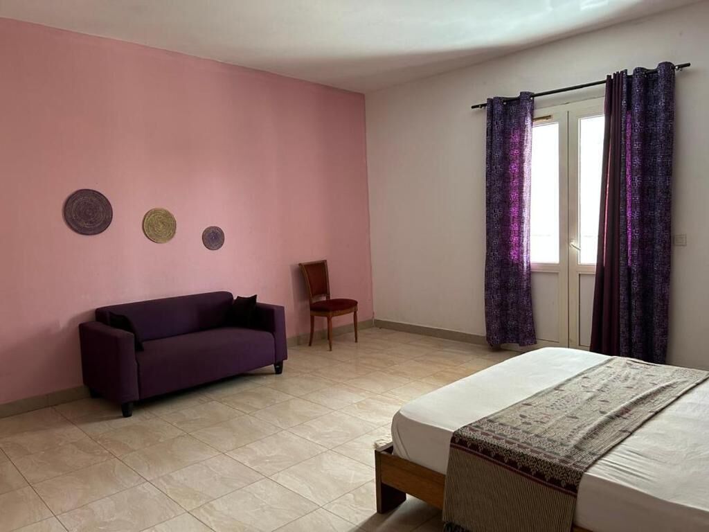 Un dormitorio con una cama, un sofá morado, una silla y una ventana con cortinas moradas.
