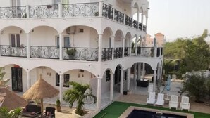 A white building with multiple balconies, a swimming pool, and outdoor seating. - Jozene House  (Ngaparou)