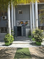 A building facade with a central entrance, flanked by two columns, and surrounded by potted plants.