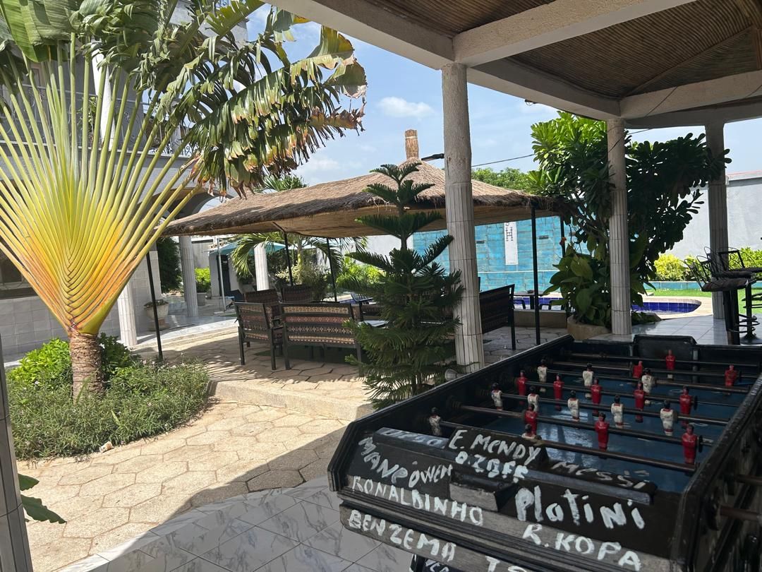 An outdoor area with a foosball table, a covered seating area, and a pool in the background.