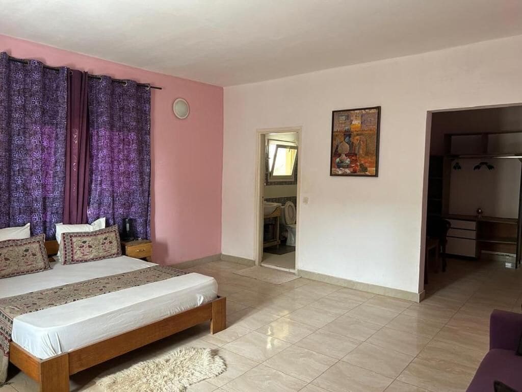 A bedroom with a bed, a wardrobe, a door leading to a bathroom, and a painting on the wall.