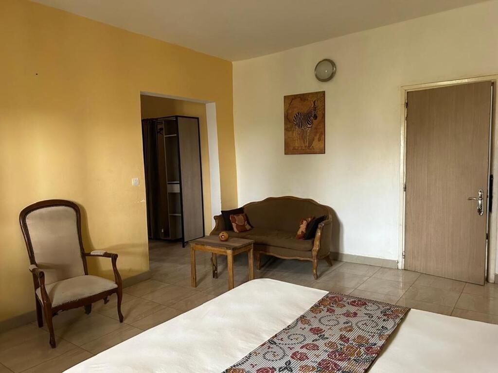 A room with a bed, a sofa, a chair, a small table, a door, and a wall clock.