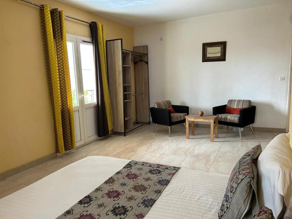 A hotel room with a bed, two chairs, a small table, a wardrobe, and a window with curtains.