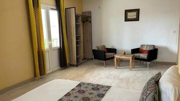 A hotel room with a bed, two chairs, a small table, a wardrobe, and a window with curtains.