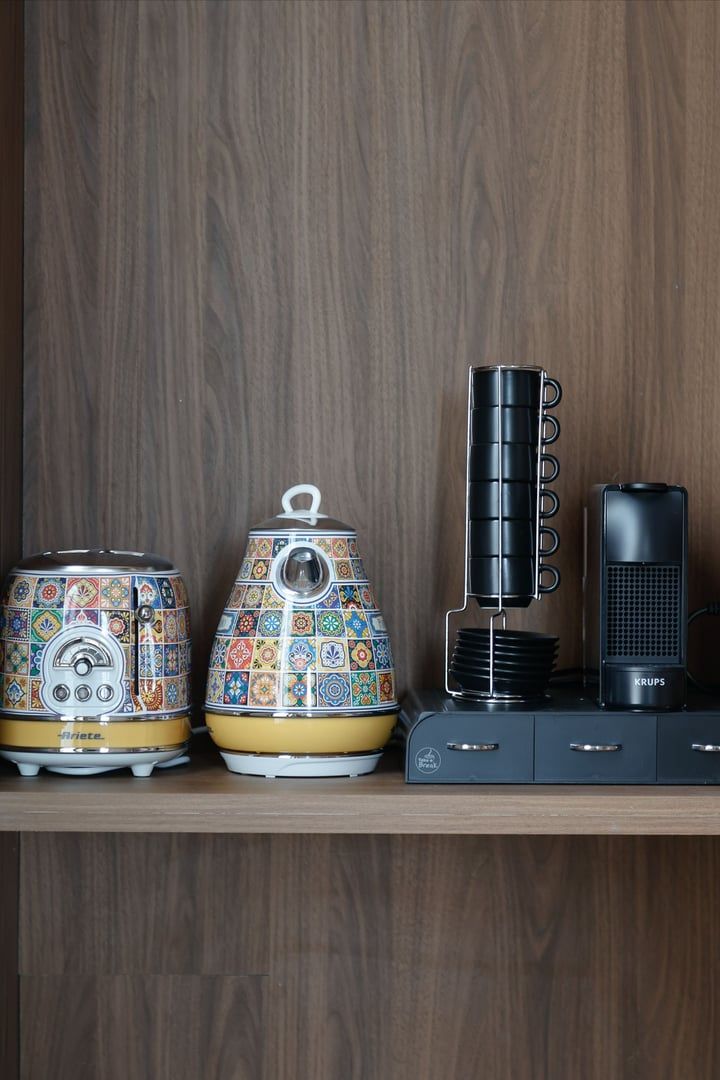 Una cocina con dos teteras de colores, una cafetera y un calentador de teteras sobre un estante de madera.