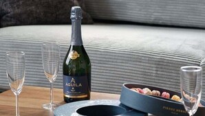 Ein Tablett mit einer Flasche Aguila-Wein, zwei Gläsern und einer Dessertschachtel auf einem Holztisch.