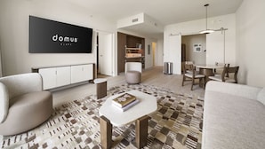 Uma sala de estar moderna com sofá, mesa de centro, área de jantar com cadeiras, TV na parede e tapete estampado.