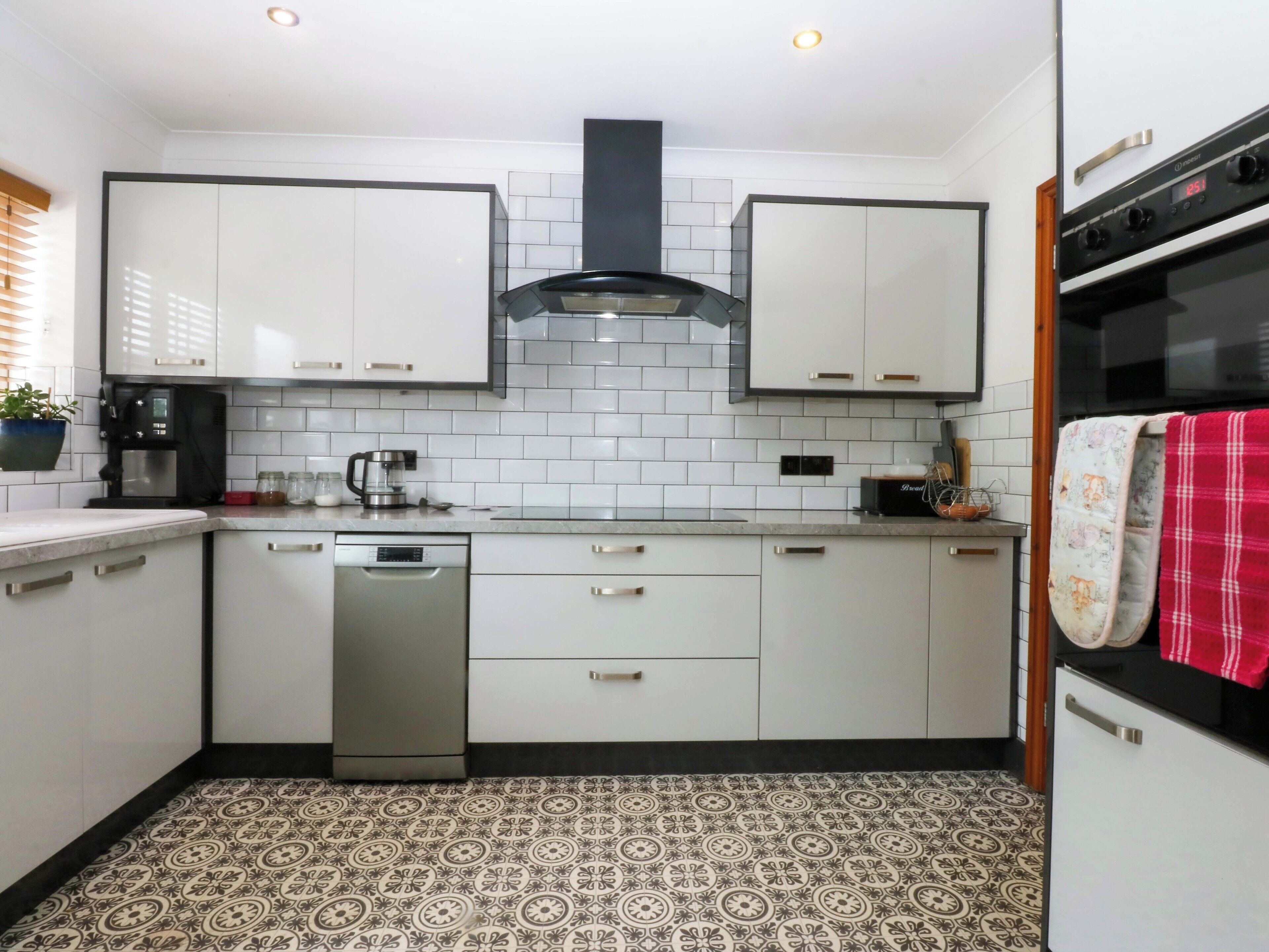 A compact kitchen with white cabinets, a dishwasher, a coffee maker, and a patterned floor.