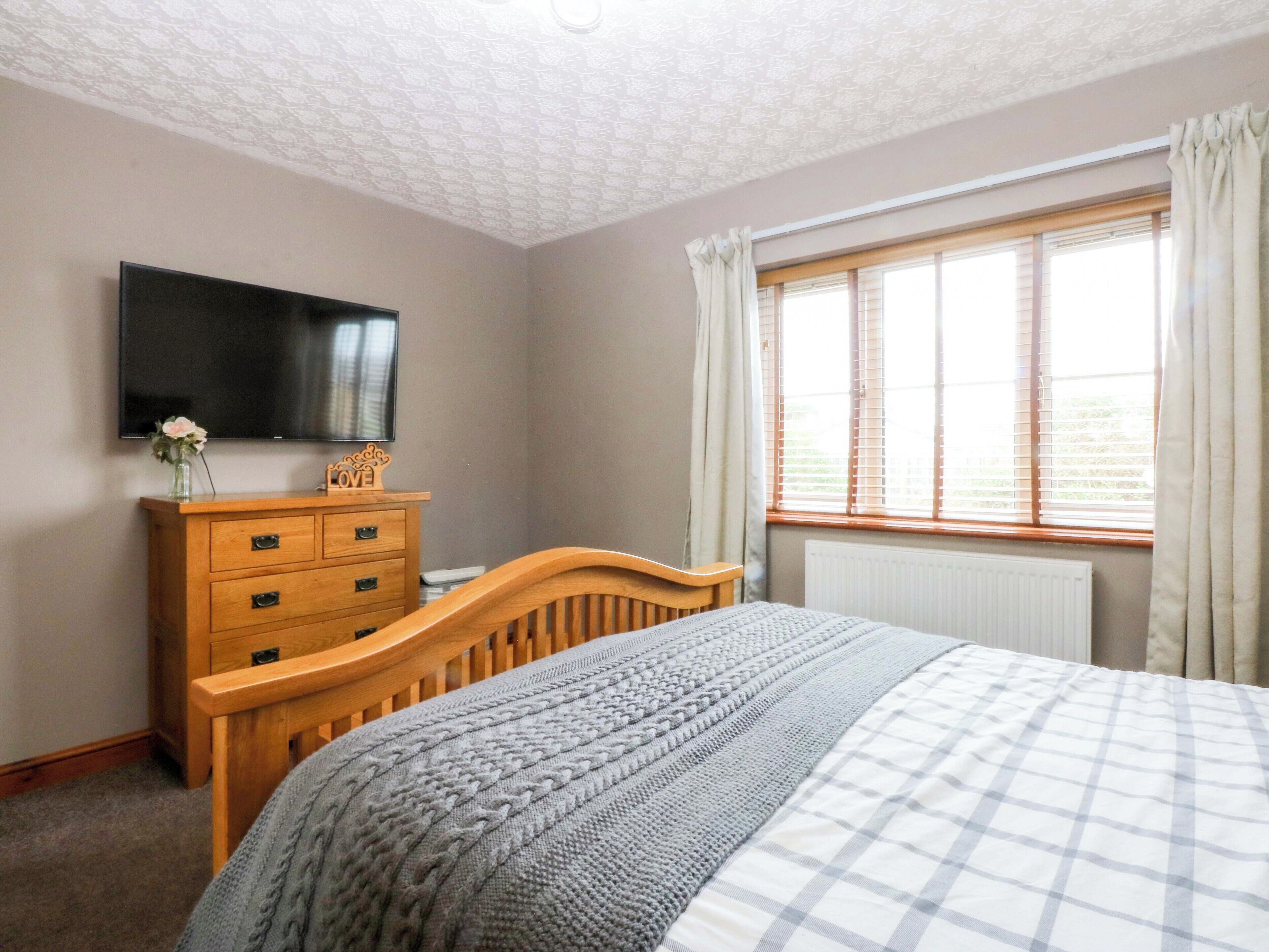 Un dormitorio con cama, cómoda, televisor de pantalla plana, ventana con cortinas y radiador.