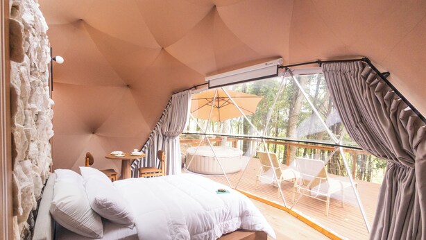 Een slaapkamer met een bed, een tafeltje en een raam met uitzicht op een terras met stoelen en een jacuzzi.