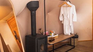 Een kamer met een houtkachel, een houten bank, een kledingrek en een spiegel.