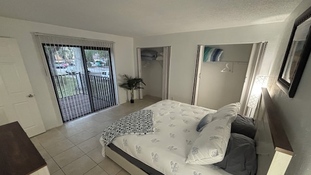 Une chambre avec un lit, une plante en pot, une porte coulissante et une vue sur l’extérieur.