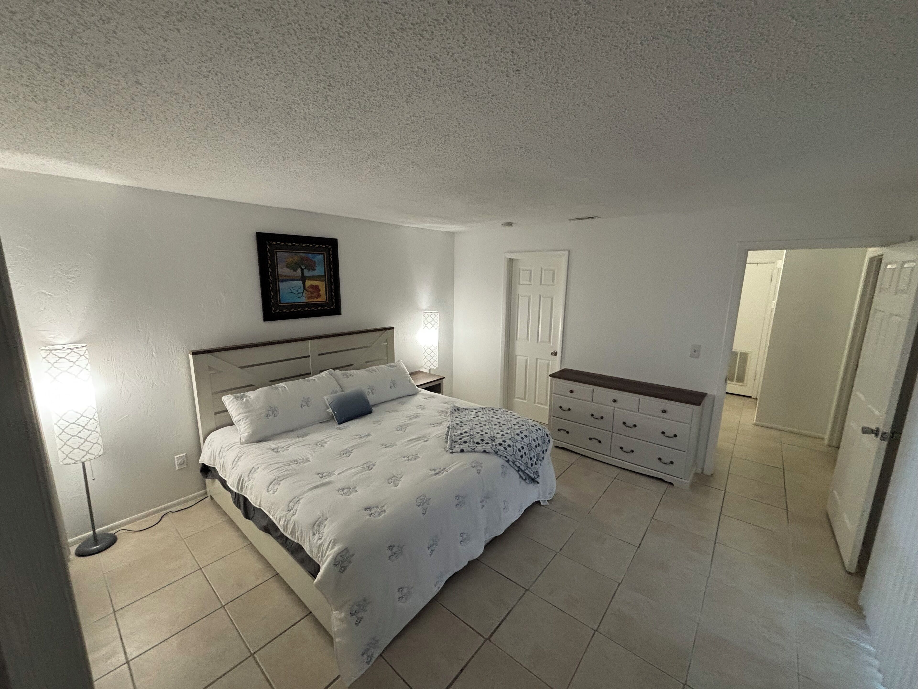 Un dormitorio con cama, mesita de noche, cómoda y una puerta.
