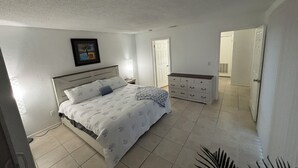 Une chambre à coucher comprenant un lit, une table de chevet, une commode et une porte donnant sur une autre pièce.