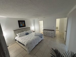 Un dormitorio con cama, mesita de noche, cómoda y una puerta que da a otra habitación.