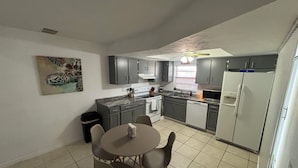 Une cuisine de taille réduite avec des meubles gris, une table à manger avec des chaises, un four à micro-ondes et un réfrigérateur.
