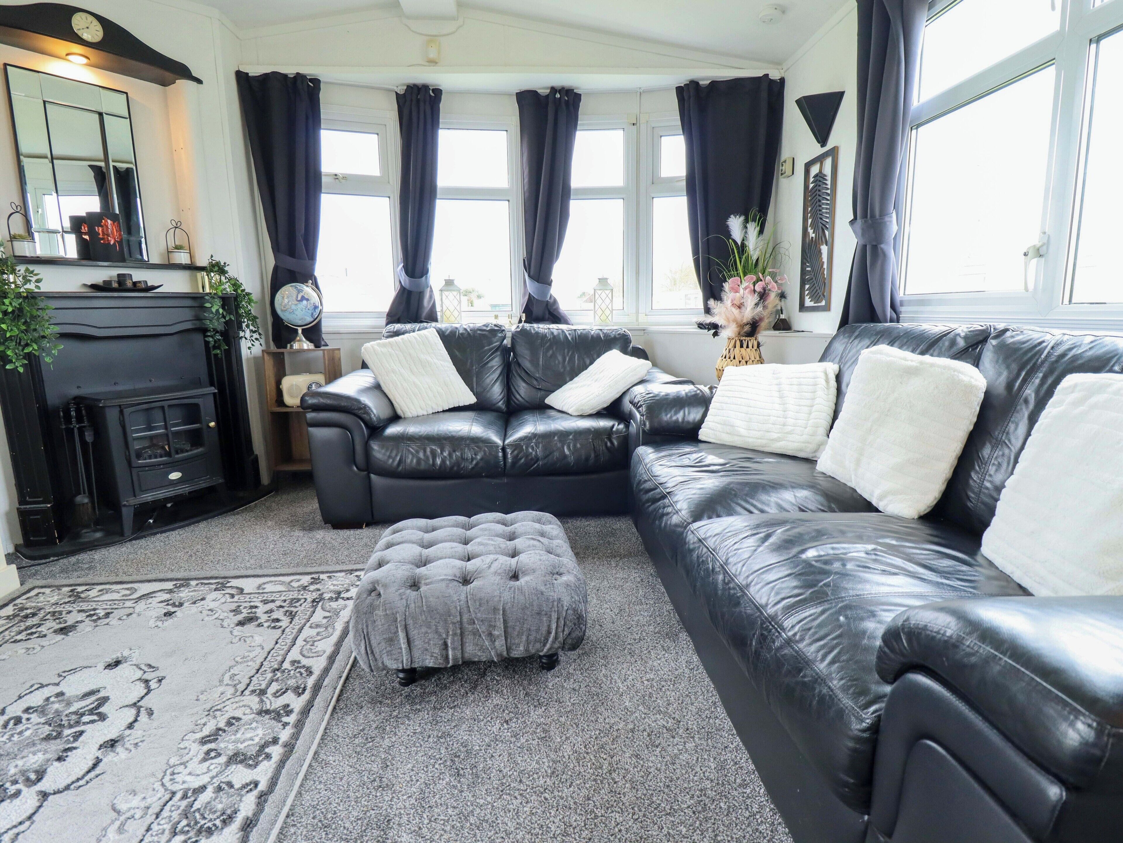 A living room with a black leather sofa, a grey ottoman, a fireplace, and a large window with curtains.