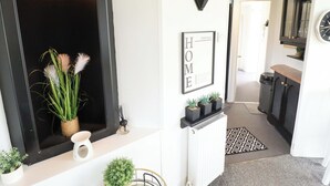 A hallway with a black-framed mirror, a framed 'HOME' sign, potted plants, a radiator, and a patterned rug. - Towervans Z11 (Mablethorpe)