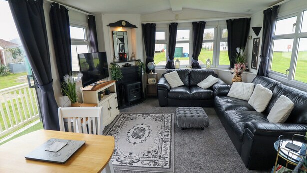 A living room with a sofa, ottoman, TV, and a small table with a laptop. - Towervans Z11 (Mablethorpe)