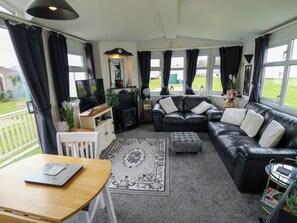A living room with a sofa, ottoman, TV, and a small table with a laptop. - Towervans Z11 (Mablethorpe)