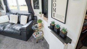 A modern living room with a black leather sofa, a small side table, a bookshelf, and a framed 'HOME' sign. - Towervans Z11 (Mablethorpe)
