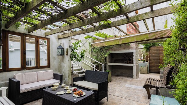 An outdoor patio with wicker furniture, a stone fireplace, and a pergola with climbing plants. - Sky Garden [Art Nouveau] Wild Terrace & Mini Pool (Montevideo)