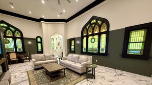 A spacious living room with a marble floor, a beige sofa, a coffee table, and a small side table. - Beautifully restored early-1900s Church. In Historic District + Pet Friendly (Tarpon Springs)