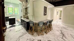 A spacious kitchen with a marble floor, a dining area with a marble table and patterned chairs, and a staircase leading to an upper level. - Beautifully restored early-1900s Church. In Historic District + Pet Friendly (Tarpon Springs)