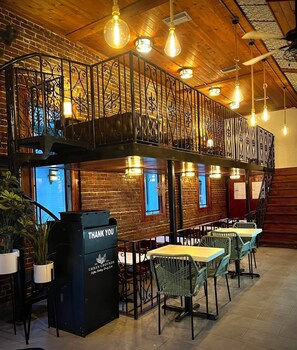 En restaurang med tegelväggar, hängande lampor och ett svart metallräcke.