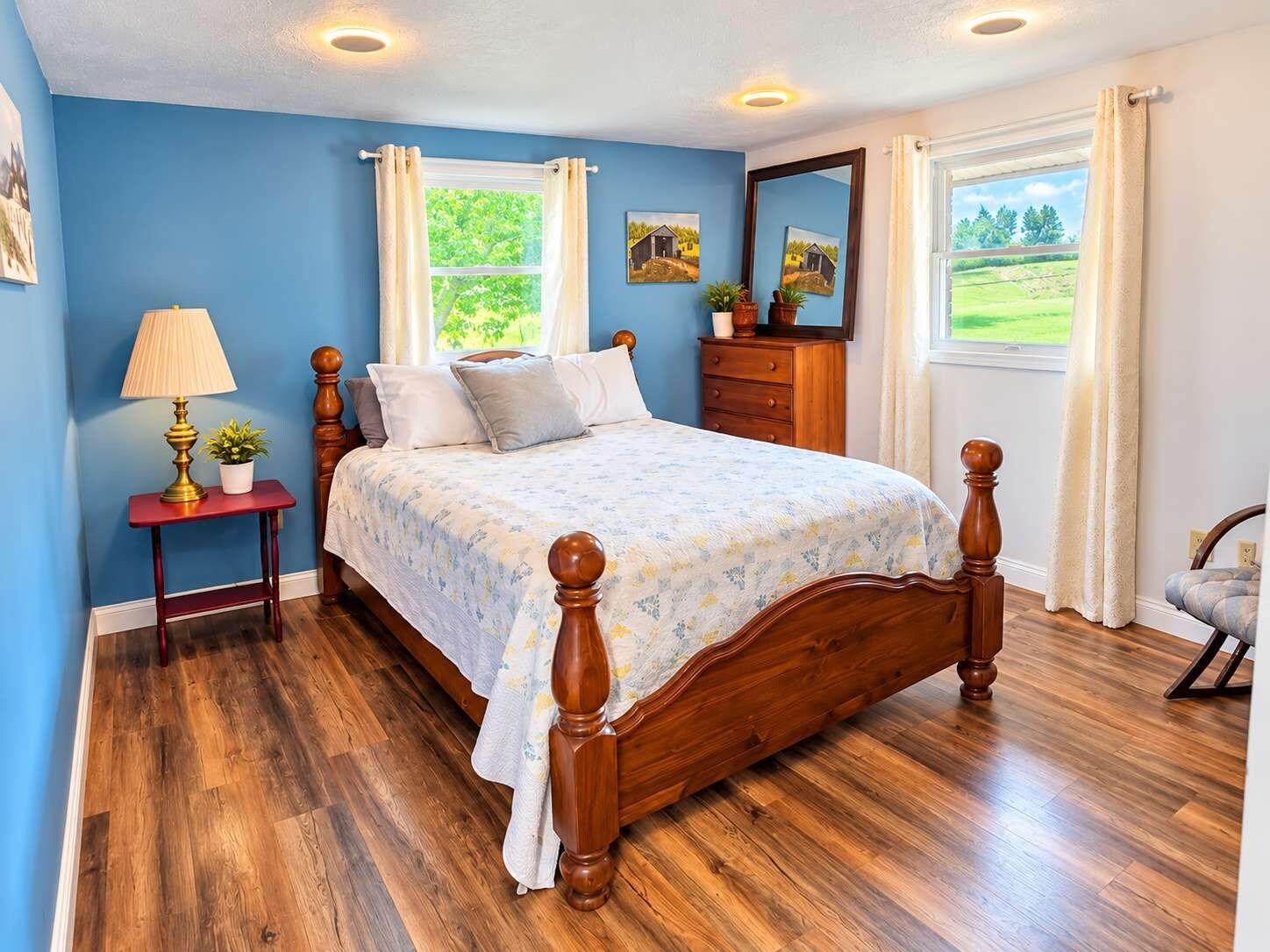 Une chambre à coucher avec un lit en bois, une table de chevet avec une lampe, une commode et une fenêtre donnant sur un paysage verdoyant.