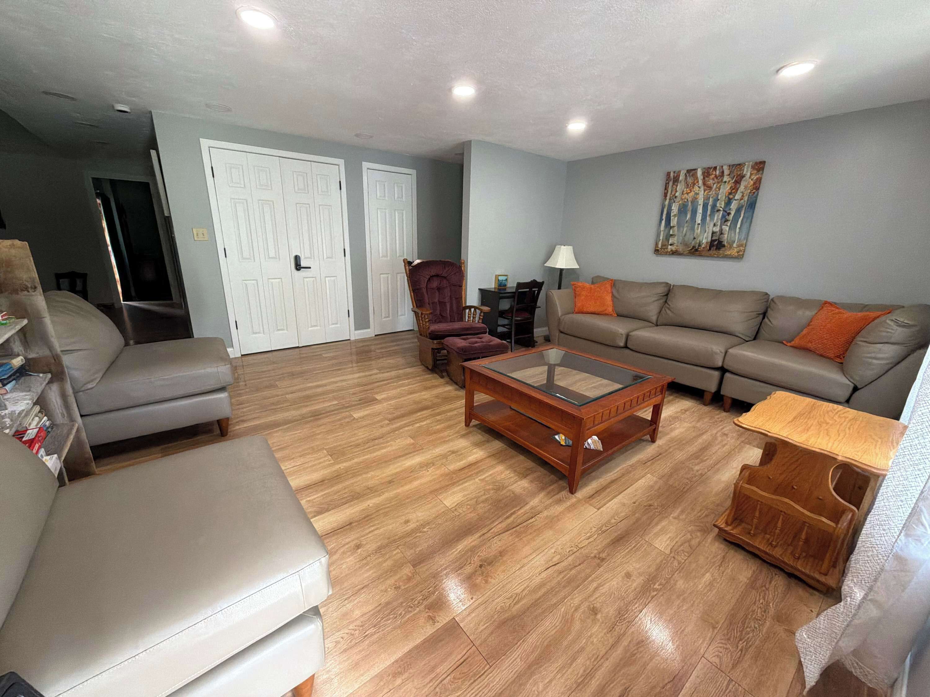 A living room with a sofa, armchair, ottoman, glass-top coffee table, and a small wooden side table.