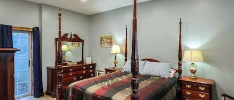A four-poster bed with a wooden finish, a dresser with drawers, a nightstand with a lamp, and a chair.