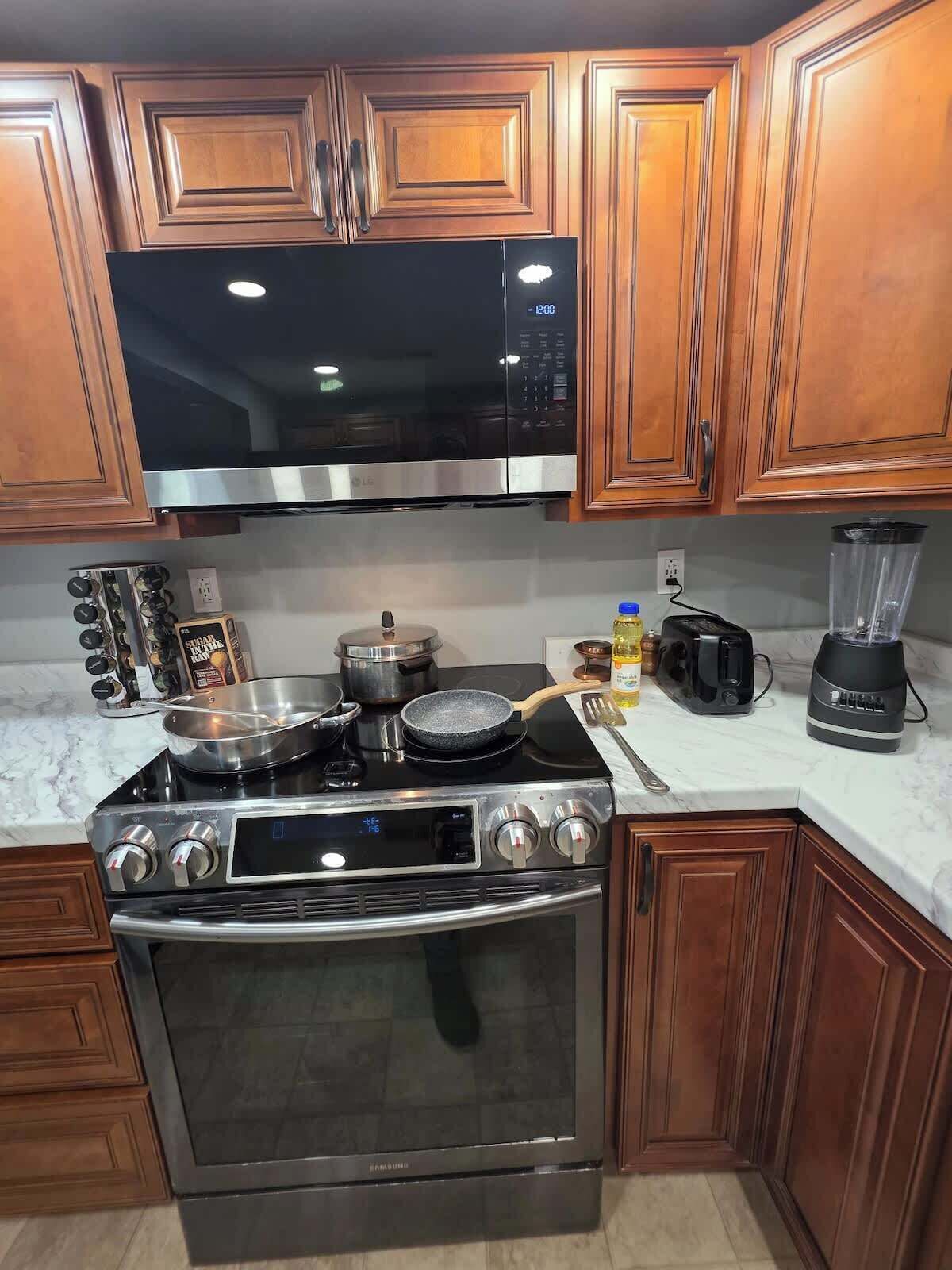 A kitchen with a stainless steel stove, microwave, and oven, wooden cabinets, and a marble countertop.